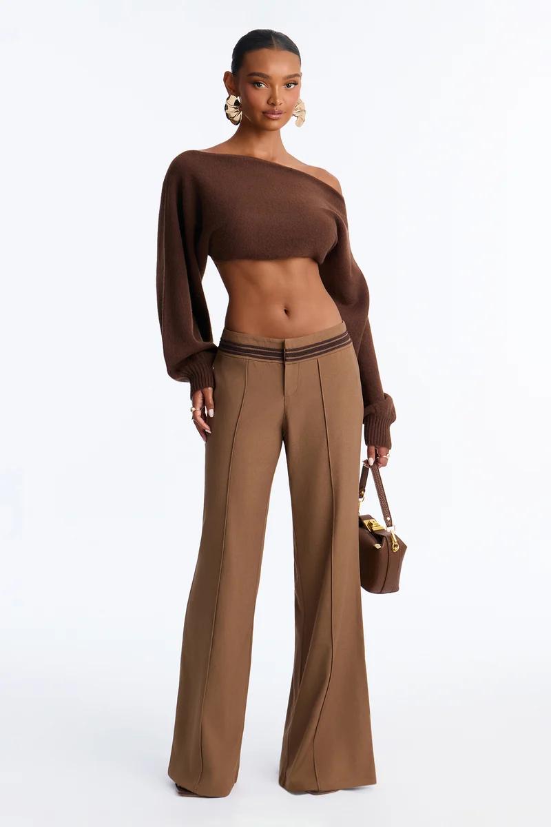 Woman in a brown off-the-shoulder crop knit sweater and low-rise wide-leg trousers.