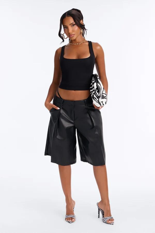 Woman in a black square neck crop top and faux leather bermuda shorts holding a zebra print clutch. Trendy summer fashion collection.