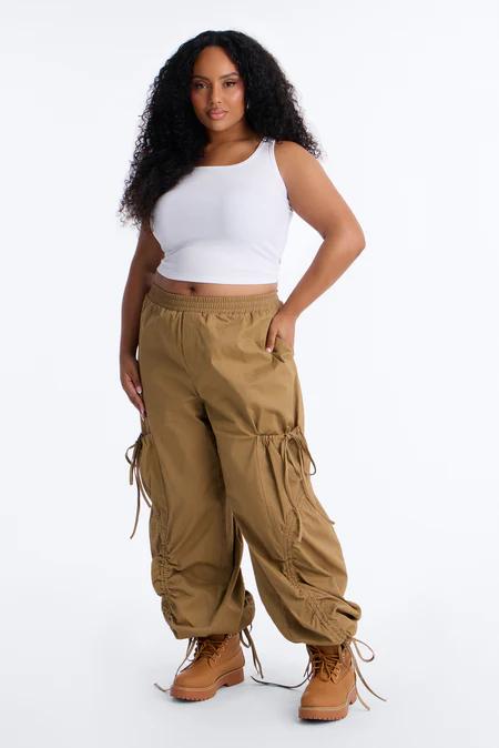 Mujer con cabello largo oscuro y rizado, vistiendo un crop top blanco, pantalones cargo marrones con cordones y botas a juego.