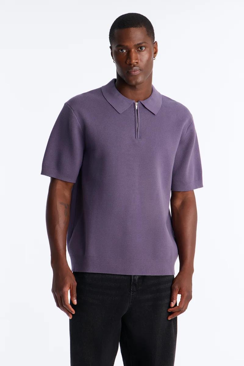 Man models a stylish short-sleeve purple knit polo shirt with a zipper and black jeans, showcasing men's casual fashion.