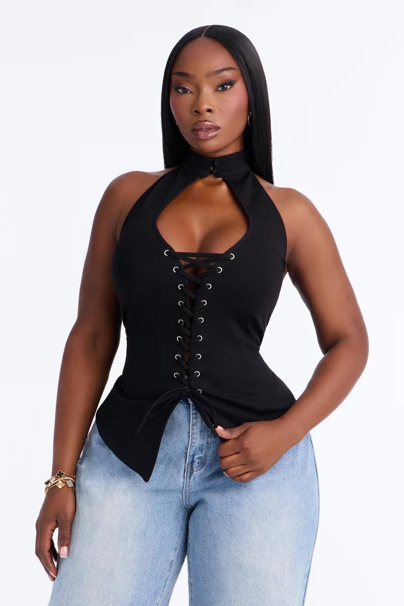 Woman wearing a black lace-up halter top with front cutout paired with light blue jeans.