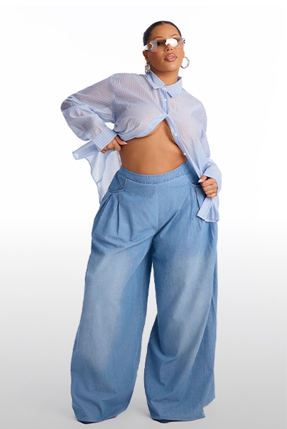 Modelo de talla grande con camisa azul claro transparente y pantalones vaqueros anchos de tiro alto, promocionando moda de primavera.