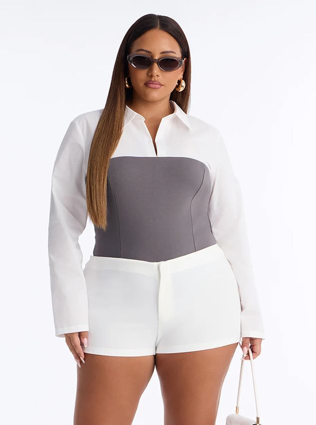 Trendy plus-size fashion featuring a model in a white long-sleeve shirt with a gray corset bodice and matching white shorts for a chic look.