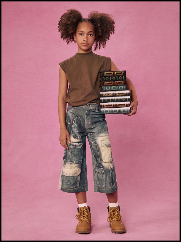 Girl in kids denim cargo pants and brown top holding books for back to school fashion collection against pink background.