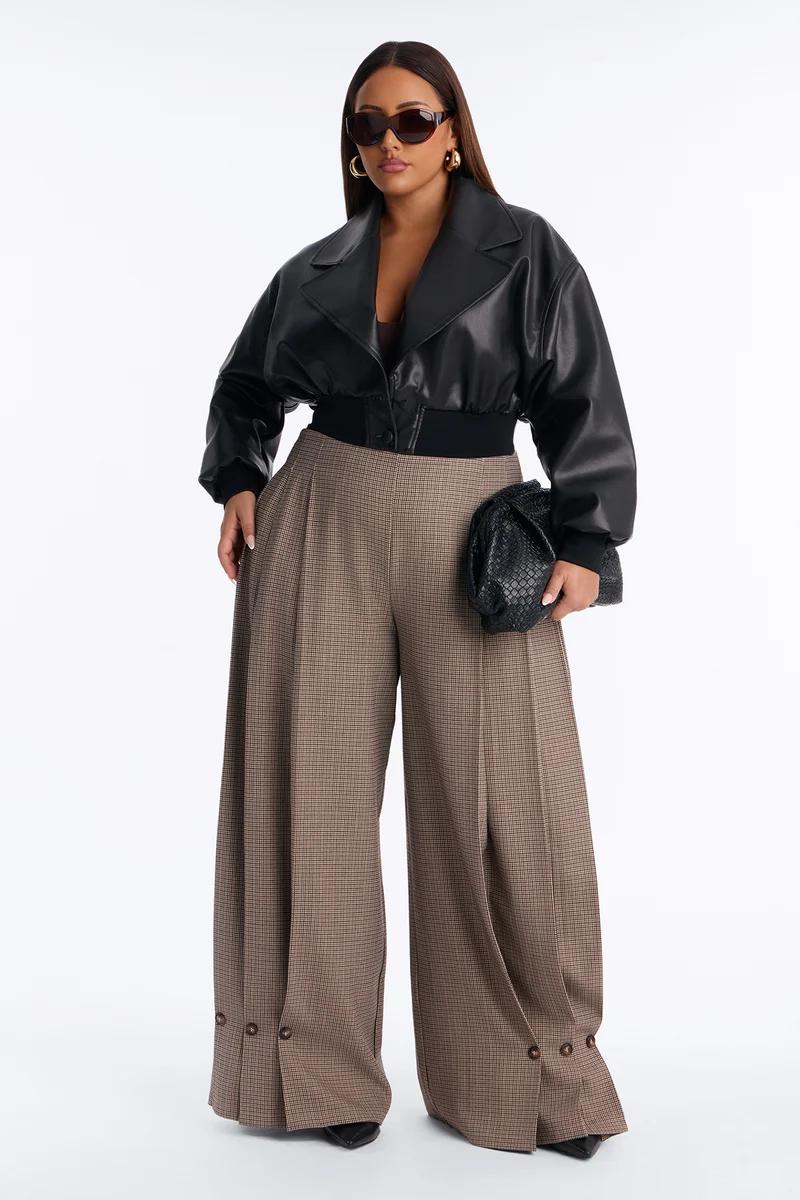 Plus-size woman in a cropped black leather jacket and brown wide-leg plaid trousers showcasing a chic, modern fall fashion collection.