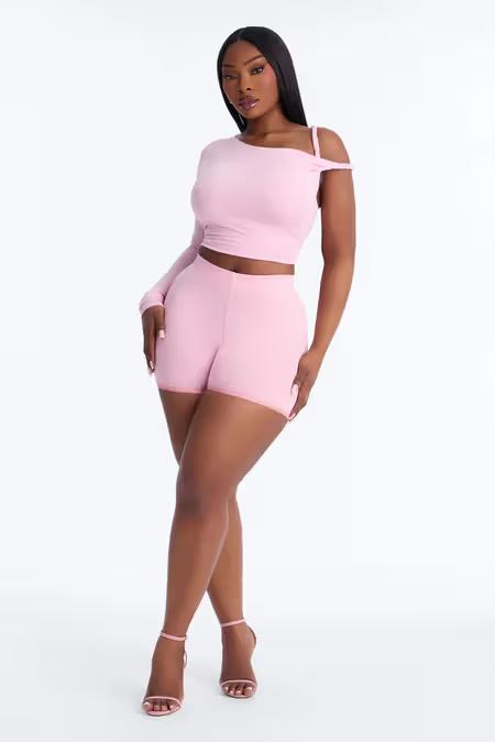 Mujer curvy con conjunto rosa de top corto de un hombro y shorts. Atuendo de dos piezas elegante.
