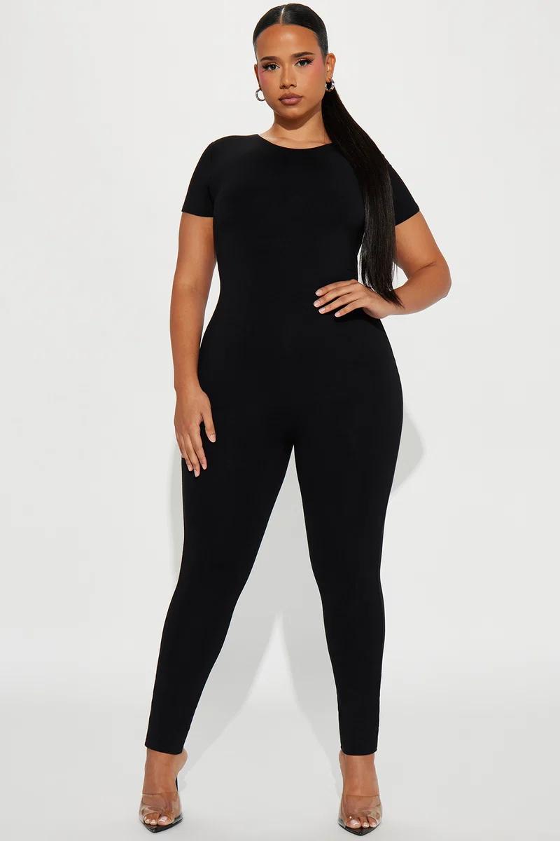 Modelo luciendo un enterizo negro plus size ajustado de manga corta, destacando esta prenda versátil y moderna para la colección de moda femenina.