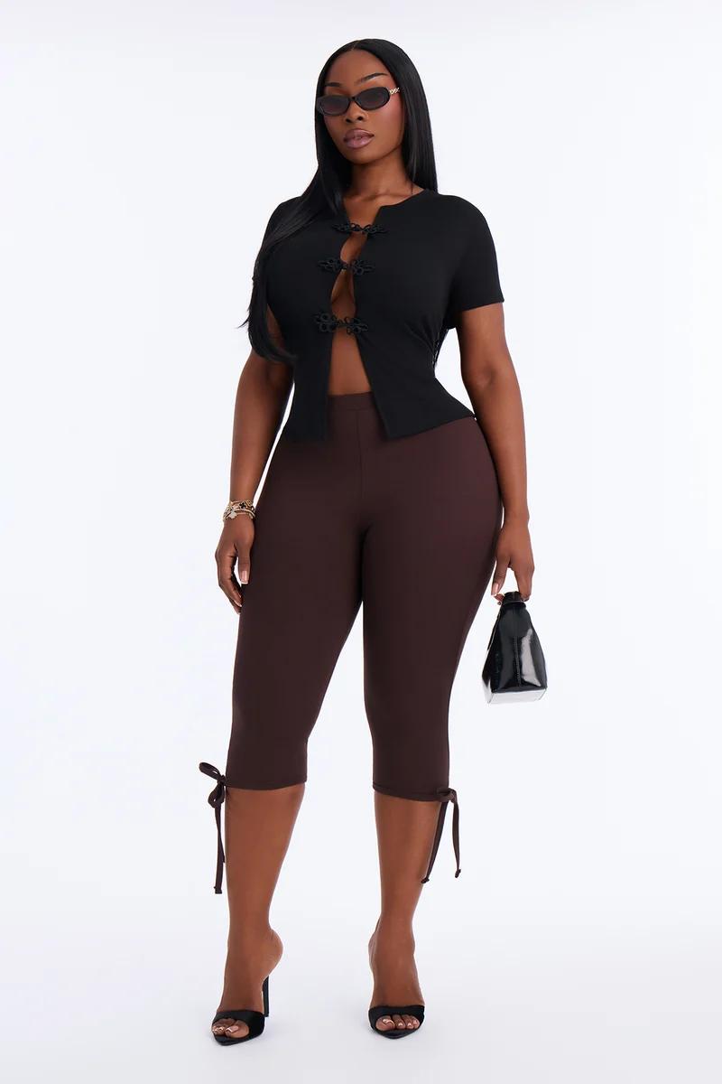 Woman in a black short-sleeve frog-closure top, brown tie-hem capri leggings, and heels.