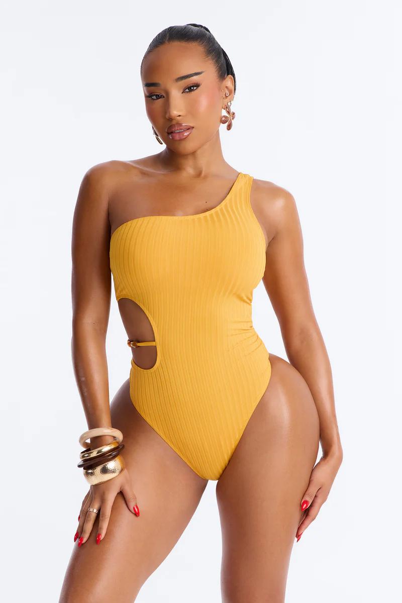 Confident woman models mustard yellow ribbed one-shoulder cutout one-piece swimsuit with gold accent.