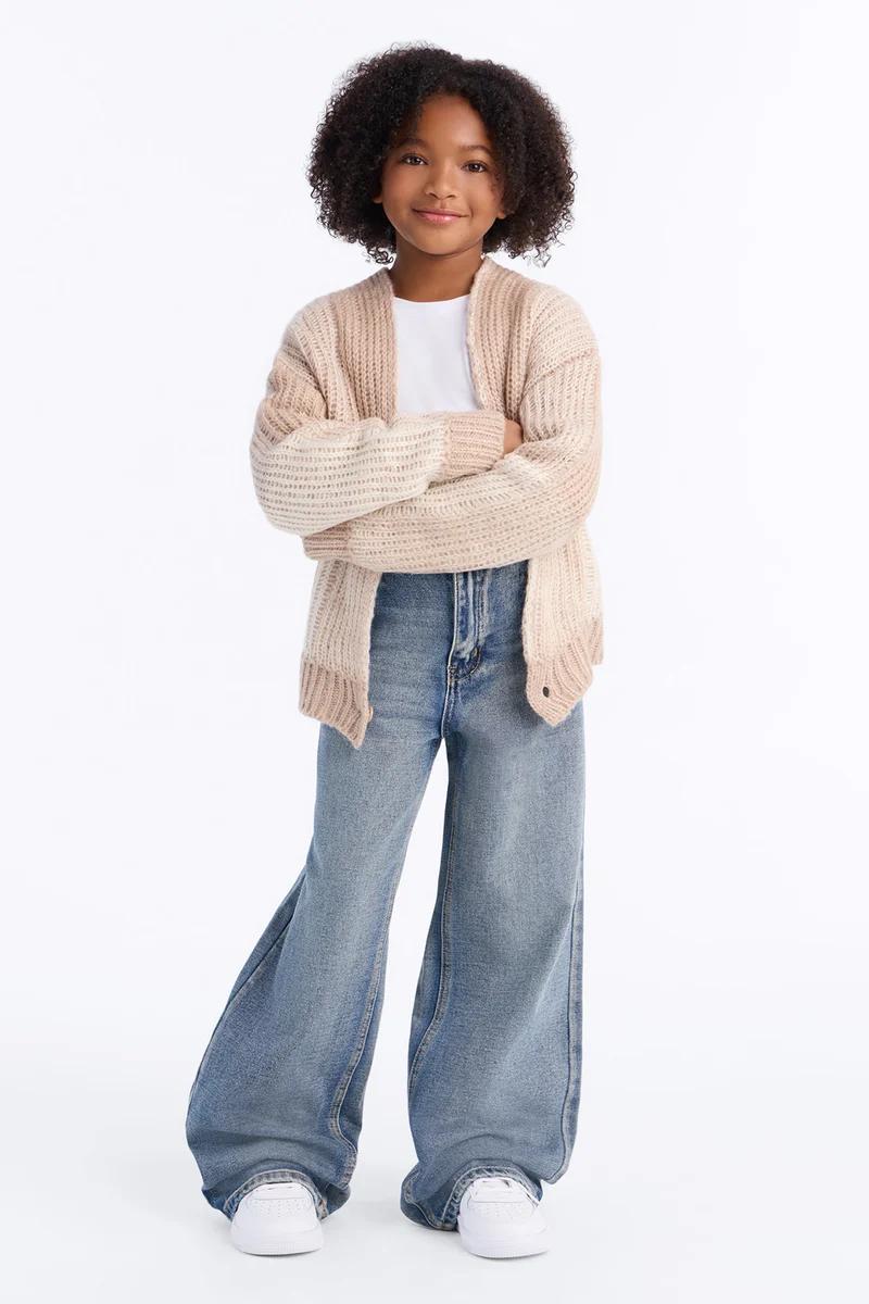 Girl wearing a beige ribbed knit cardigan, white t-shirt, and wide-leg jeans.
