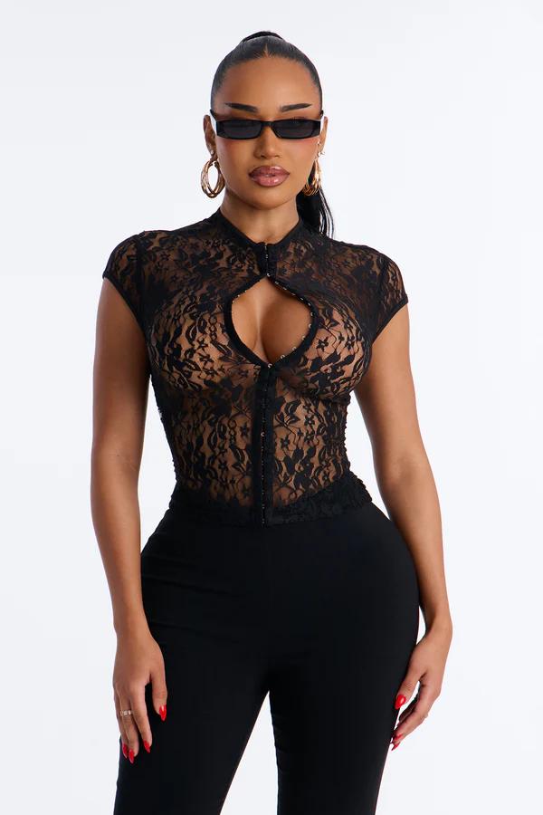 Woman models a black sheer lace top with a keyhole cutout, hook-and-eye closure, and black pants. Wears rectangular sunglasses and gold hoop earrings.