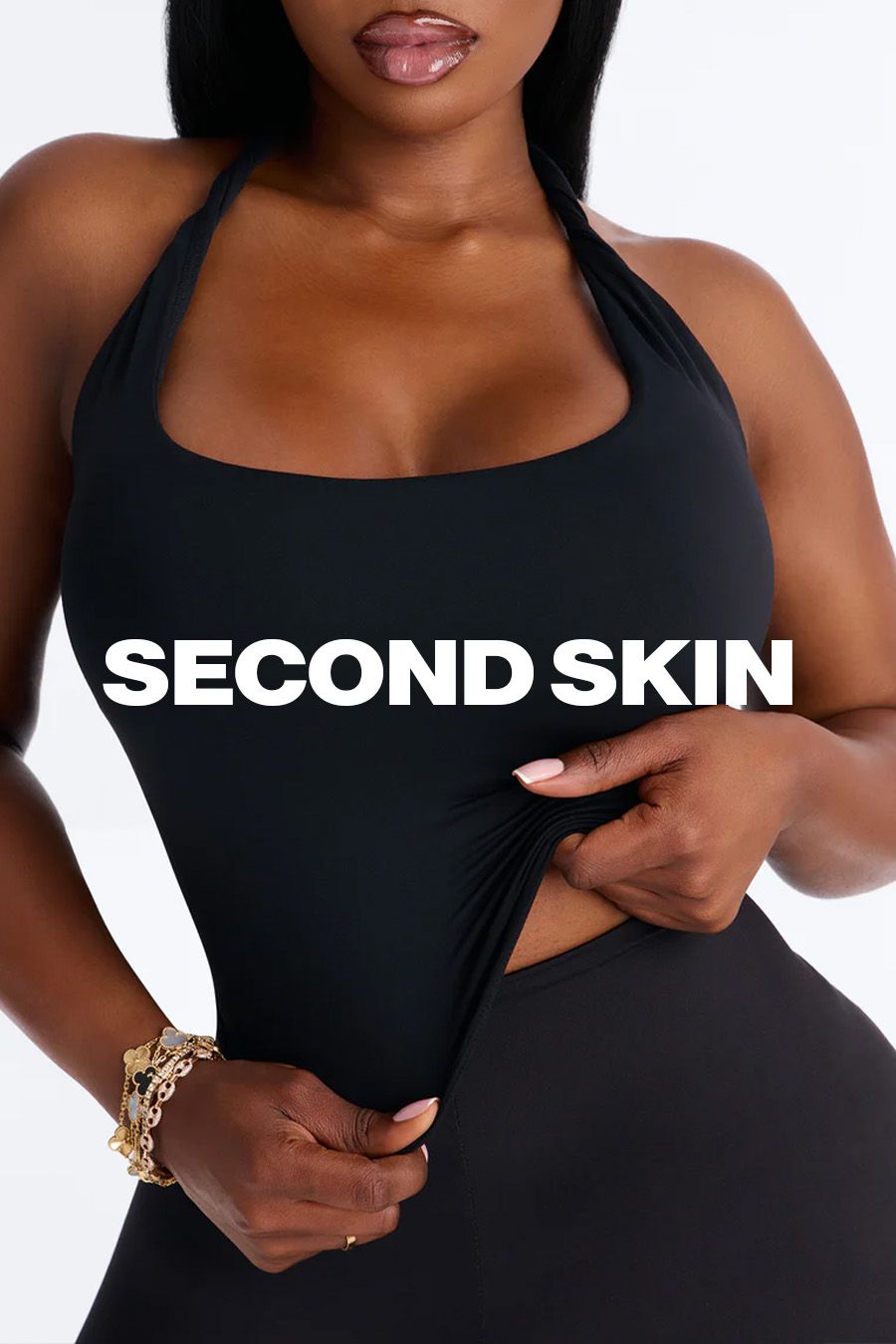 Woman stretching a black halter bodysuit from the Second Skin shapewear collection to show its stretchy, form-fitting compression fabric.