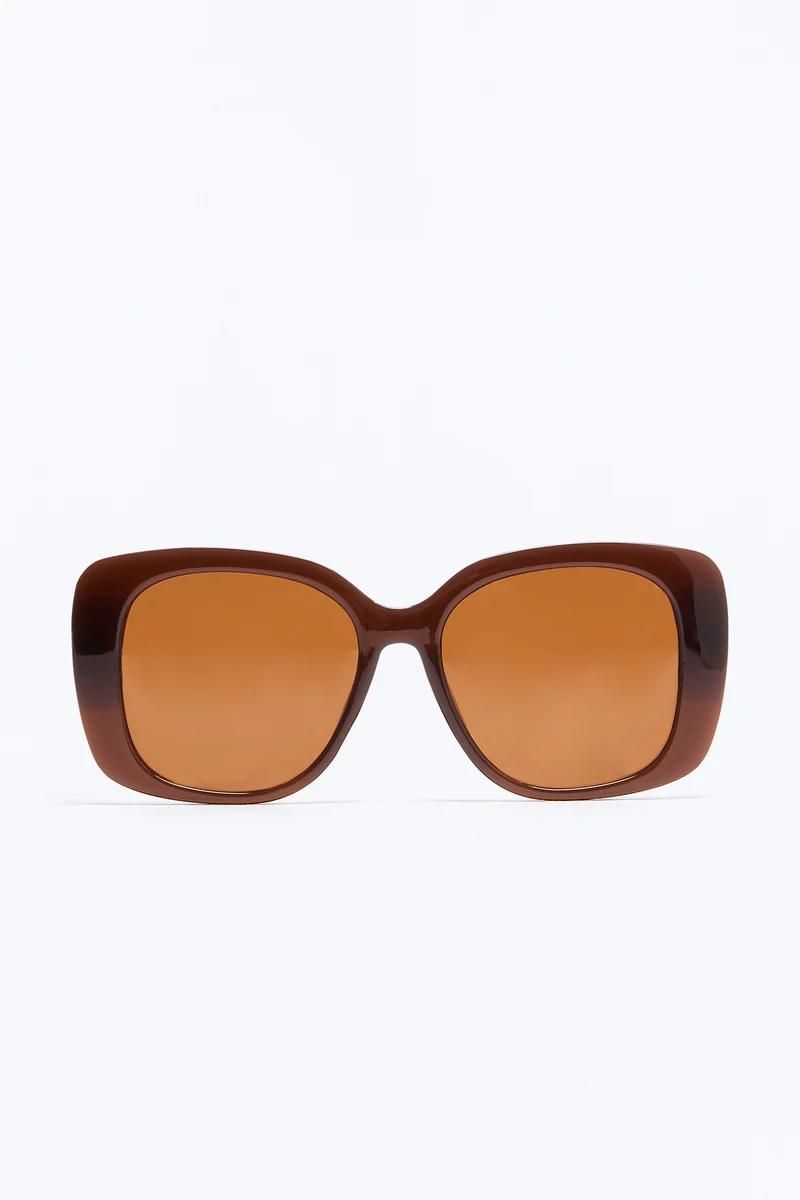 Gafas de sol cuadradas y grandes en color marrón con lentes ámbar, de la nueva colección de accesorios de verano sobre fondo blanco.