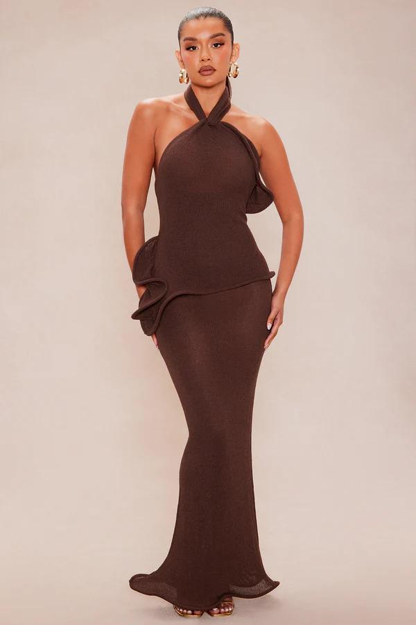 Elegant woman in a fitted brown ribbed knit halter maxi dress with a twisted neckline and sculpted waist detail. Discover new party styles.