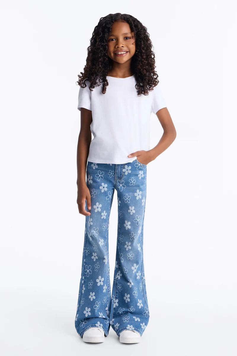 Niña sonriente con camiseta blanca, vaqueros azules acampanados con estampado de margaritas. Estilo casual infantil.