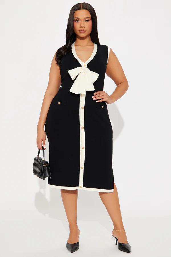 Stylish plus size woman in a black sleeveless midi dress with cream trim, front buttons, and a large bow. Perfect for a chic look.
