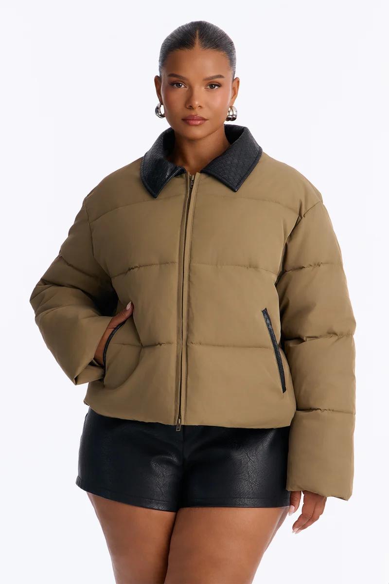 Plus size woman wearing a brown puffer jacket with a black faux leather collar.