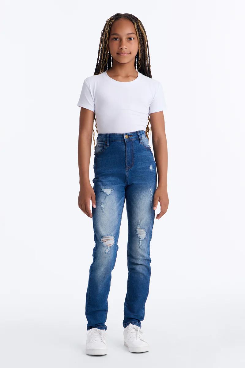 Niña con camiseta blanca, jeans azules rotos de tiro alto y zapatillas blancas.