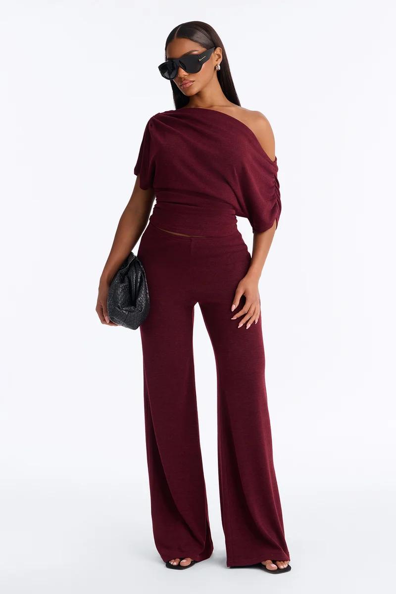 Model wears a chic maroon knit matching set with a draped one-shoulder top and wide-leg pants, showcasing a new trendy loungewear collection.