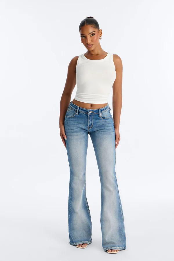 Mujer usando jeans campana de tiro bajo azul y crop top blanco, presentando una nueva y moderna colección de mezclilla retro y casual.