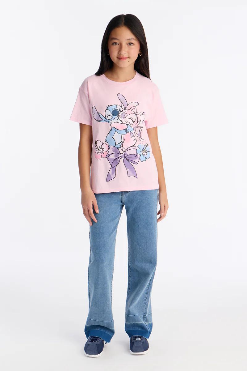 Young girl in a pink Stitch and Angel graphic t-shirt, blue denim jeans, and navy sneakers, promoting kids' casual fashion.