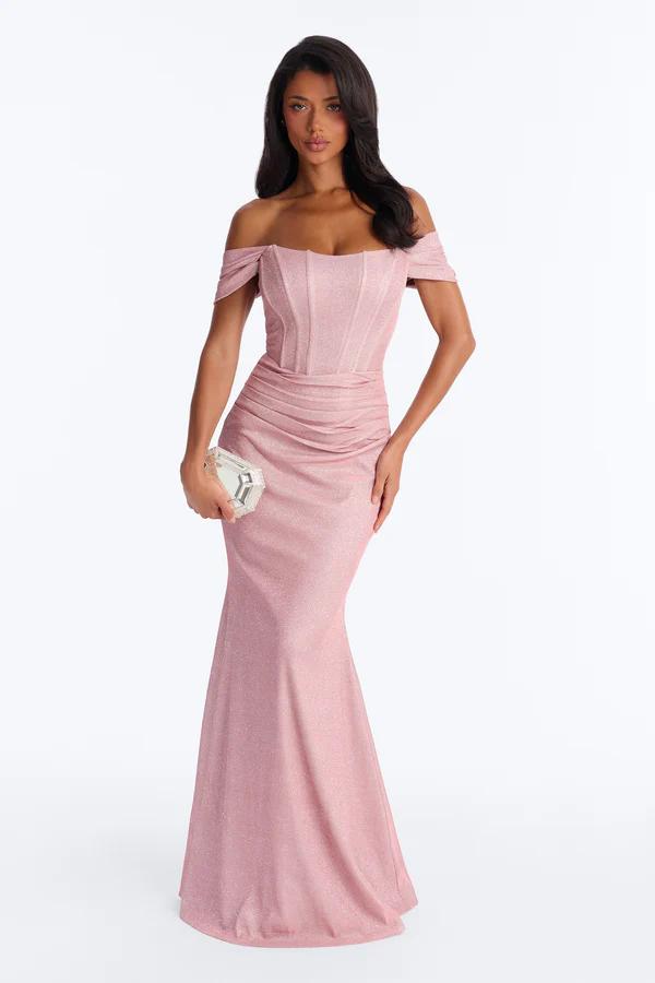 Elegant woman modeling a shimmering rose pink off-shoulder gown with a ruched, fitted bodice and flowing mermaid skirt, holding a silver clutch. Ideal formal wear.