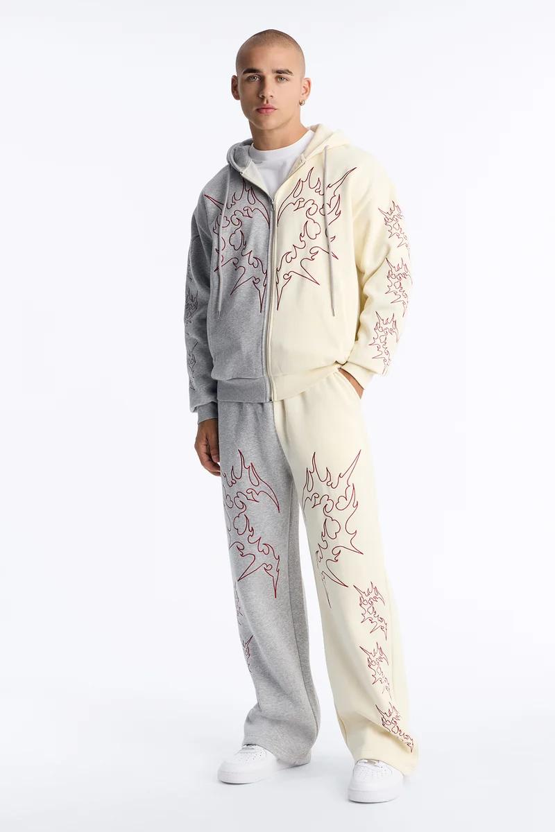 Man models a trendy two-tone grey and cream tracksuit with red flame outlines. Perfect for men's streetwear loungewear collection.