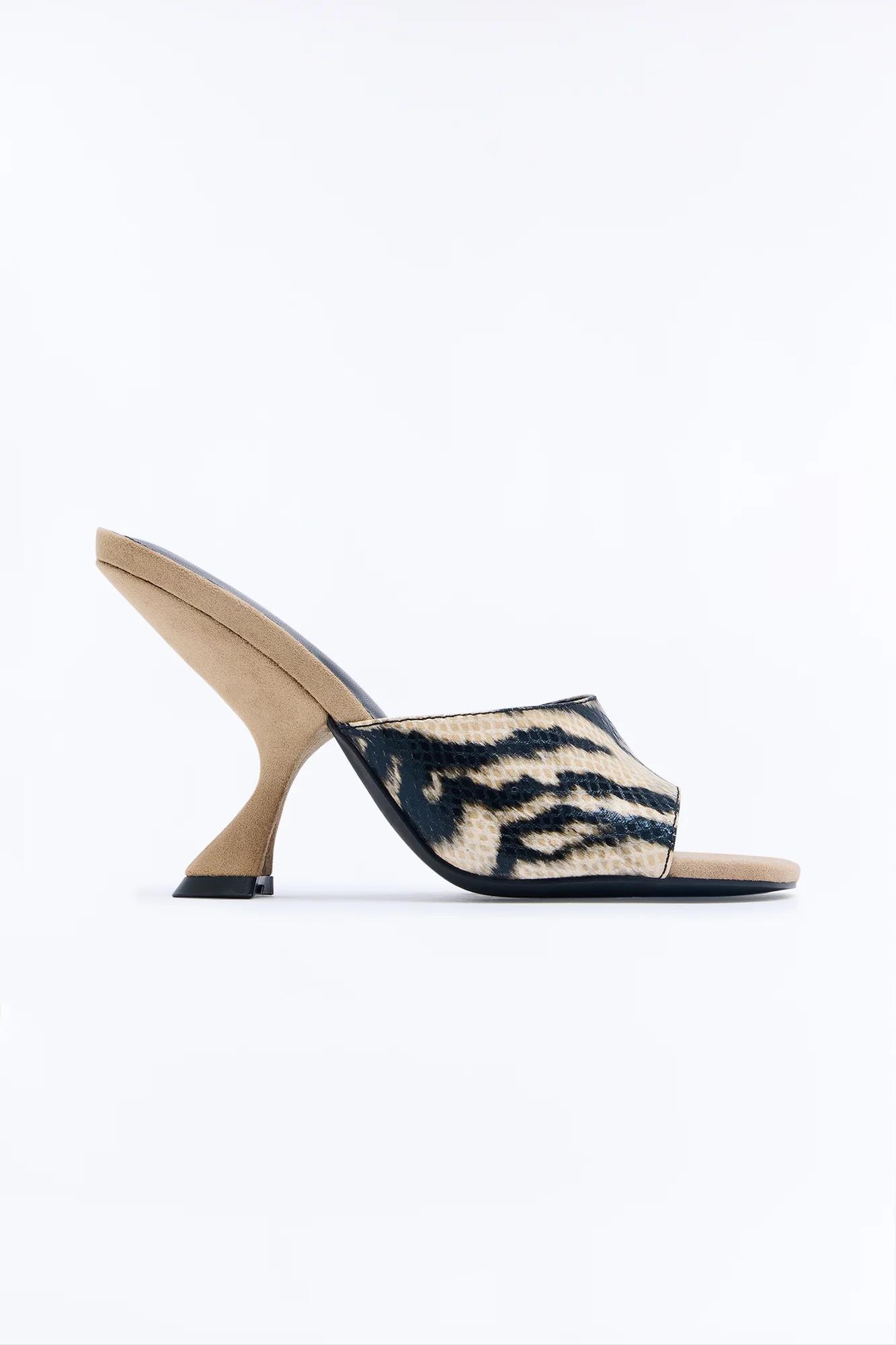 Mule beige elegante con tacón esculpido curvo. Presenta una llamativa tira con estampado de tigre negro y camel. Plantilla beige.