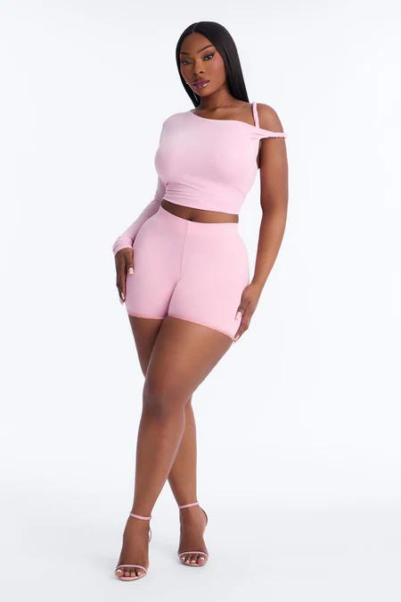 Curvy woman in pink one-shoulder crop top & shorts set. Stylish two-piece outfit for women.