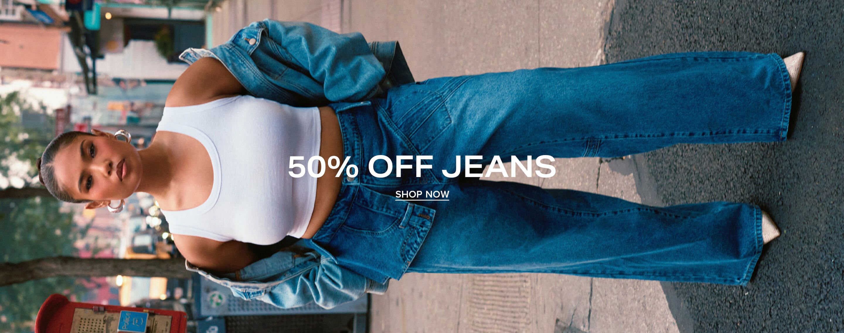 Woman in wide-leg blue jeans and a white tank crop top standing on a city street, promoting a 50% off women's denim fashion sale.