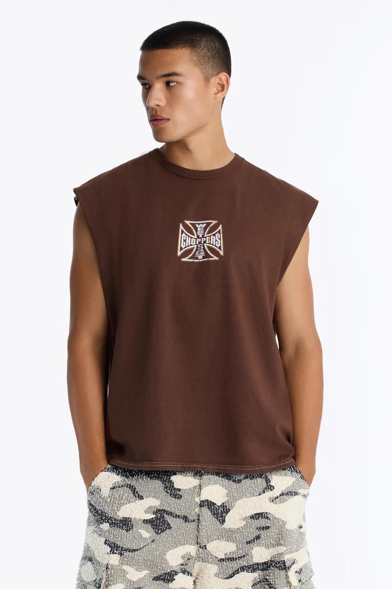 Man in a brown Choppers graphic sleeveless t-shirt, paired with camouflage shorts, showcasing new men's casual streetwear style.