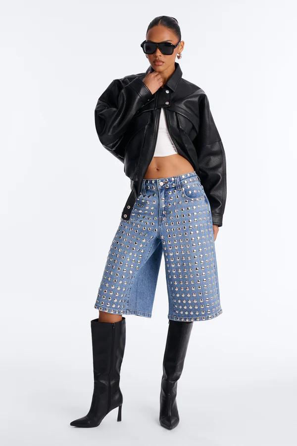 Modelo con chaqueta de cuero negra, top blanco, culottes vaqueros azules con tachuelas y botas altas negras de tacón. Con gafas.