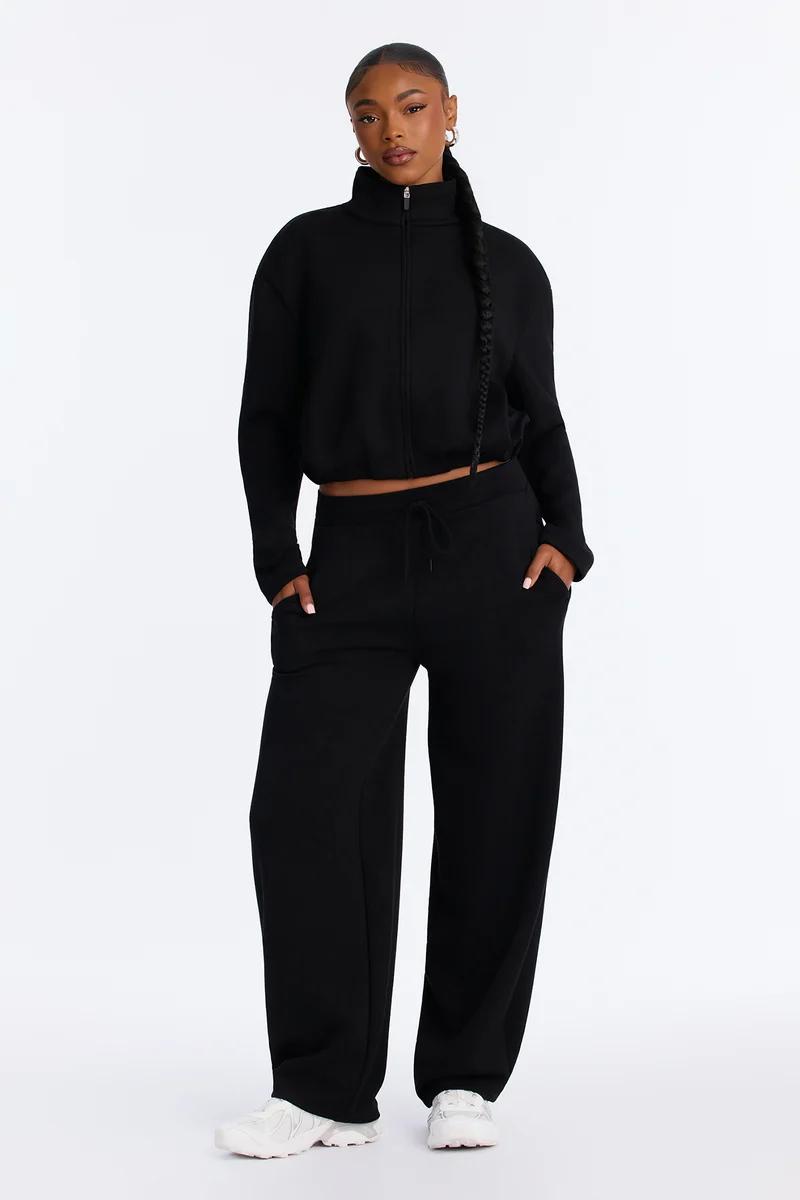 Woman wearing a black cropped zip-up jacket and matching wide-leg sweatpants.
