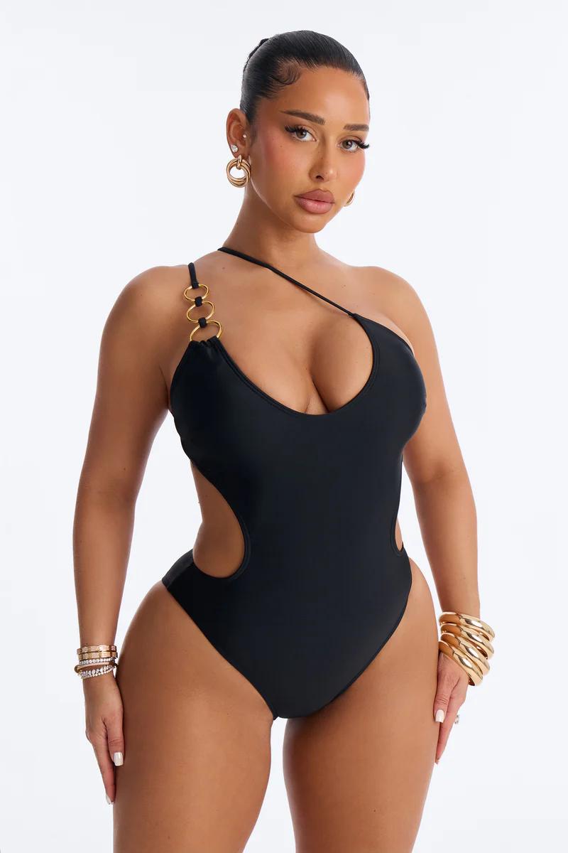 Glamorous model in black one-piece swimsuit with chic side cutouts, gold hardware & one-shoulder design.