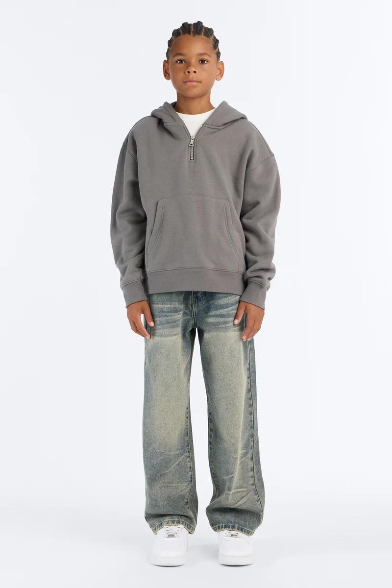 Boy wearing an oversized grey half-zip hoodie and loose washed jeans.