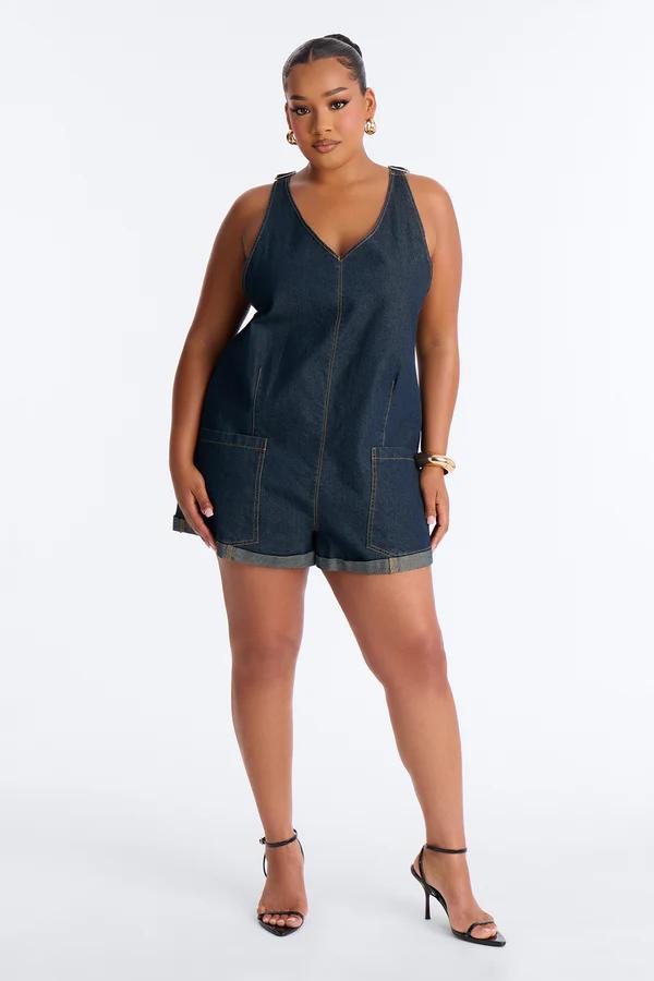 Mujer en mameluco de mezclilla oscuro talla grande con bolsillos, tacones negros y joyas doradas, perfecto para un look casual de primavera.