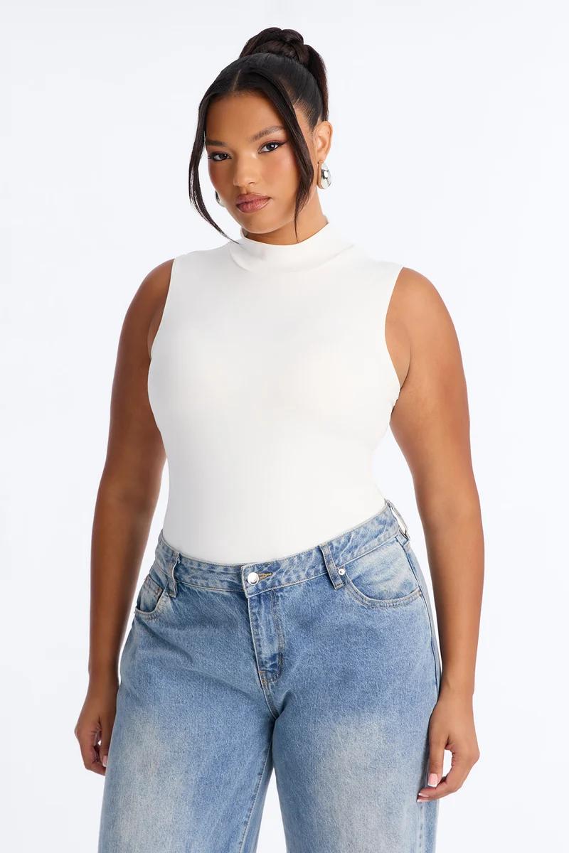 Plus size model in a white sleeveless mock neck top and light wash blue jeans.