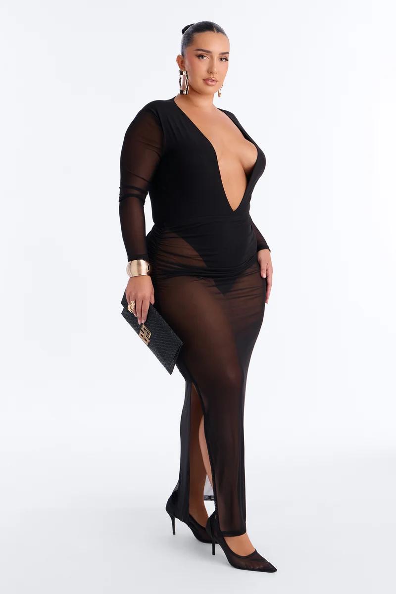 Model poses in a sheer black maxi dress with a deep plunge neckline and long mesh sleeves for an evening fashion collection showcase.