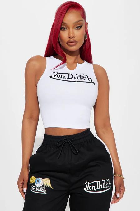 Stylish woman with red hair wearing a white Von Dutch logo crop top and black track pants, highlighting trendy streetwear.