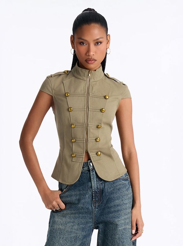 Model wears a sleeveless military style khaki top with gold buttons and blue jeans, promoting a trendy new women's fashion collection.