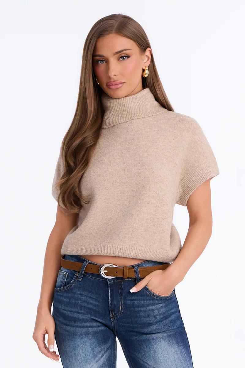Woman wearing a beige short-sleeve turtleneck knit sweater with blue jeans.