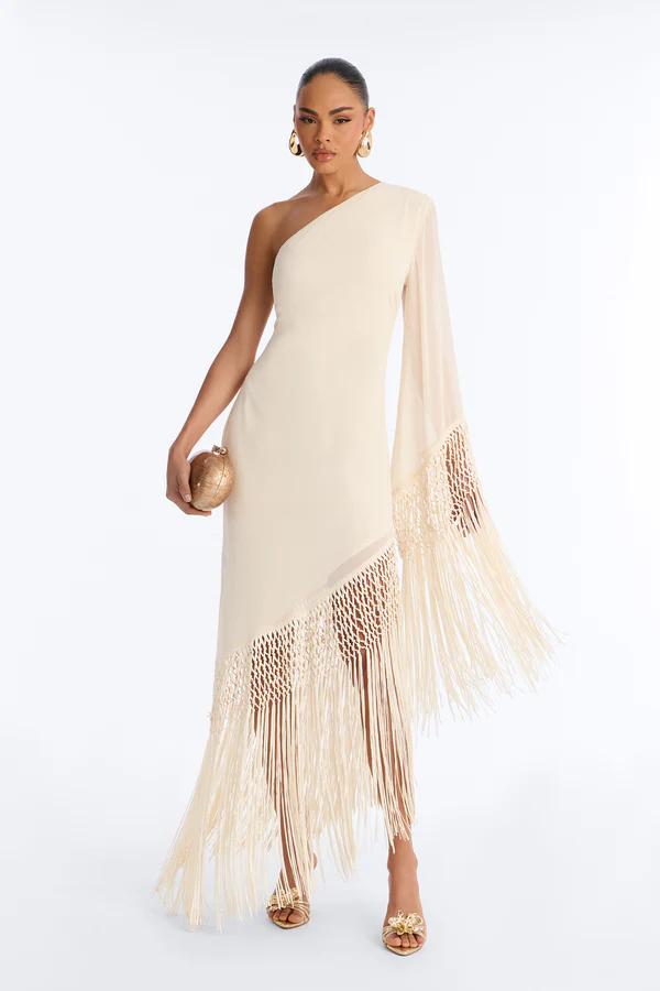 Woman posing in a two-piece brown and cream striped knit outfit with tiered fringe, a waist cutout, gold arm cuff, and braided clutch bag.