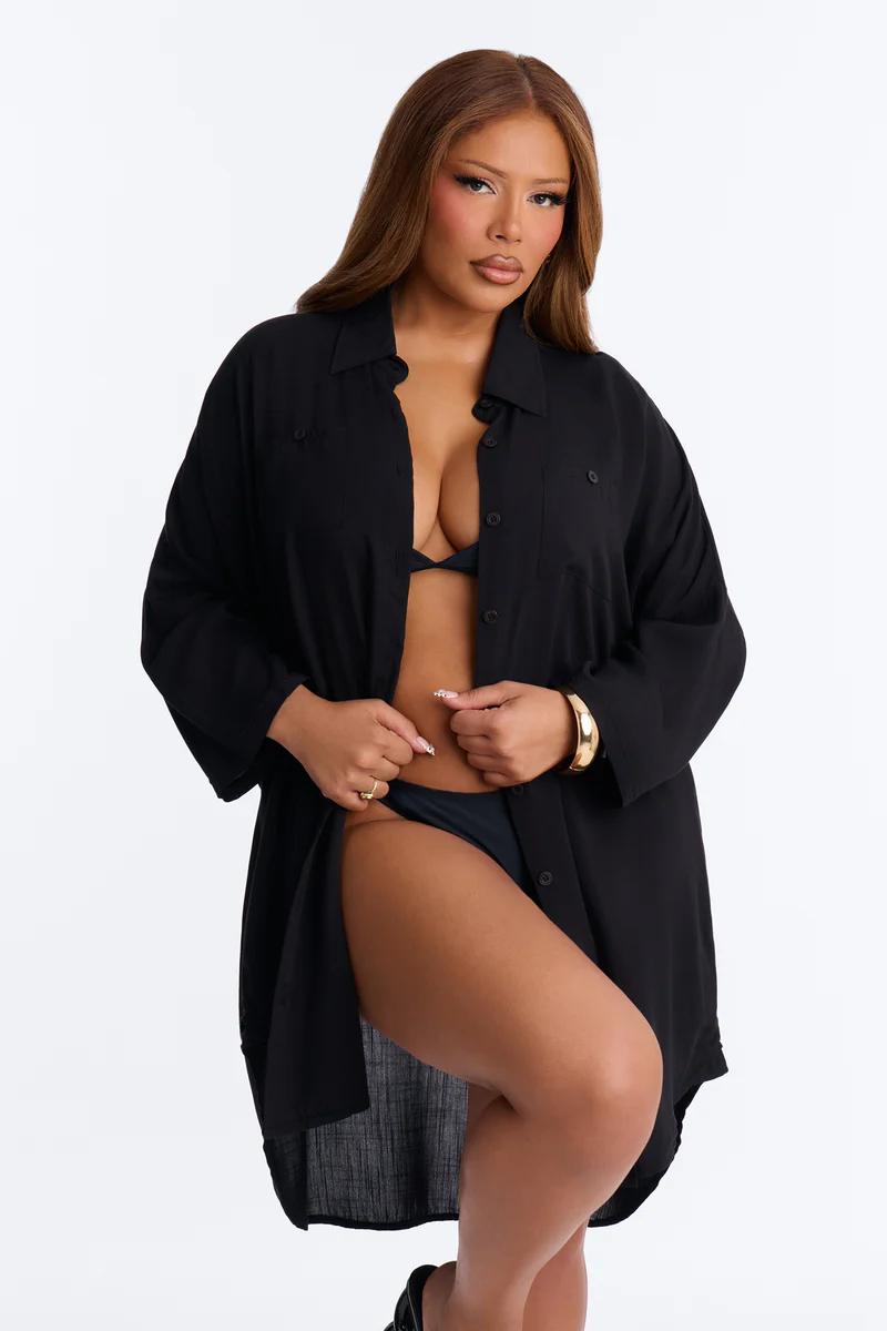 Plus size woman in black bikini & oversized cover-up shirt. Confident resort wear fashion.