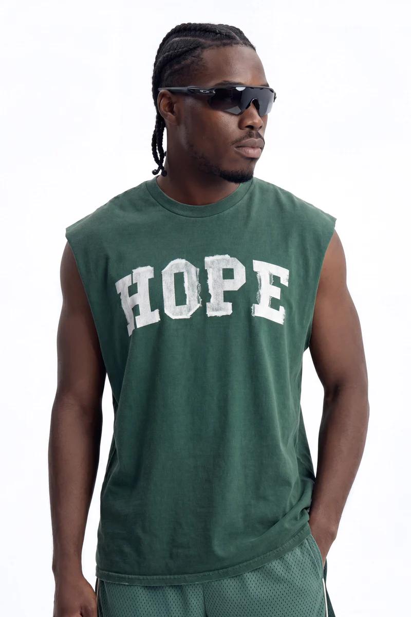 Man in dark green sleeveless "HOPE" tee and matching mesh shorts, wearing black sunglasses. Ideal for casual men's fashion and summer style.