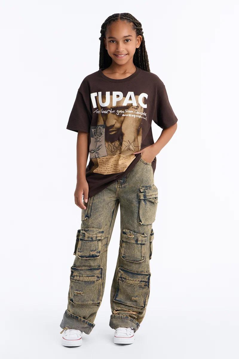 Young girl in a brown Tupac graphic t-shirt and green baggy cargo pants, kids streetwear fashion.