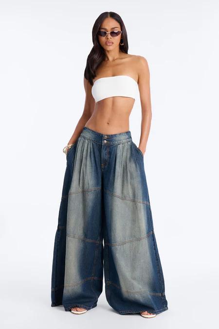 Woman wearing white strapless crop top and fashionable oversized, pleated patchwork denim palazzo pants with sunglasses. Standing.