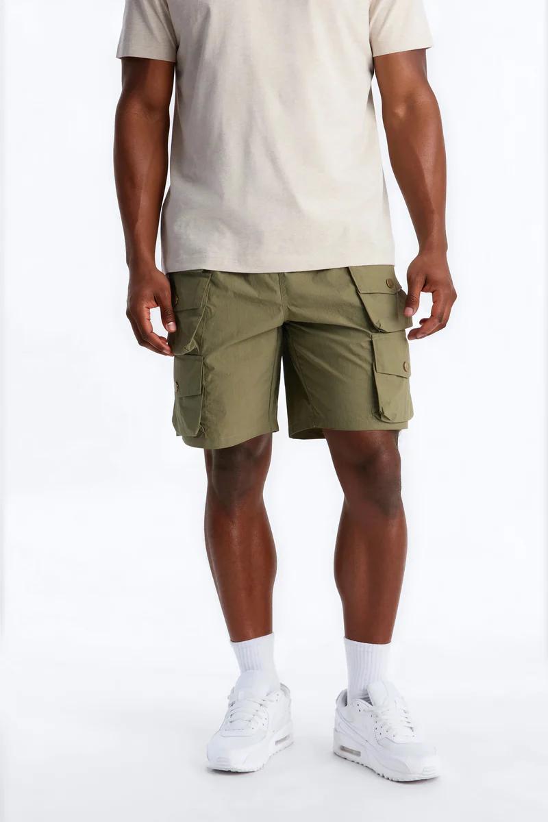 Man in a light beige t-shirt and stylish olive green cargo shorts, paired with white sneakers, ideal for men's summer fashion.