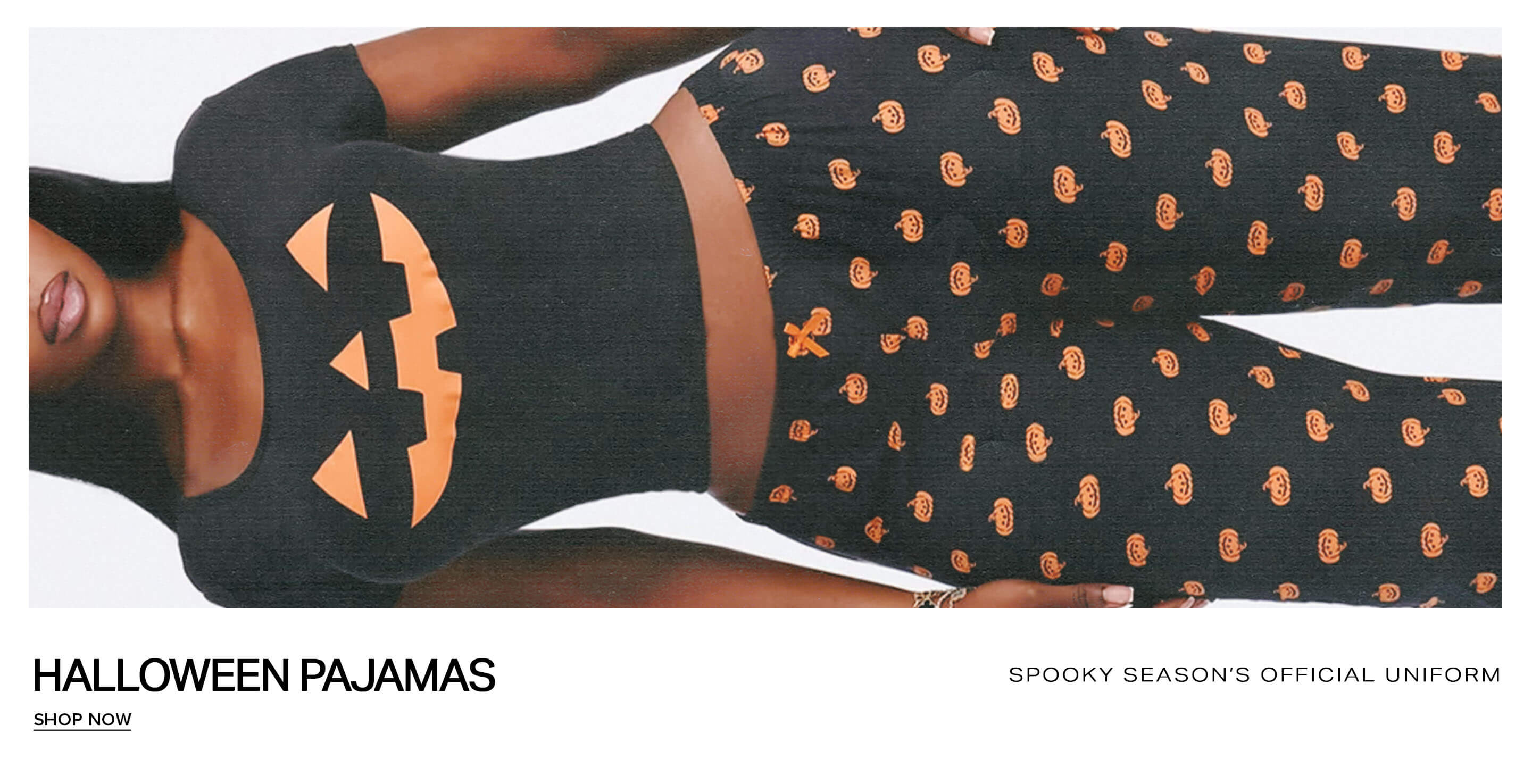 Woman wearing black Halloween pajamas with a jack-o'-lantern top and pumpkin pants, promoting the spooky season loungewear collection.