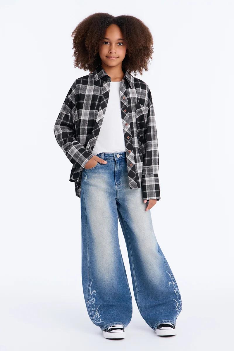 Niña con camisa de franela a cuadros en blanco y negro y vaqueros de pierna ancha.