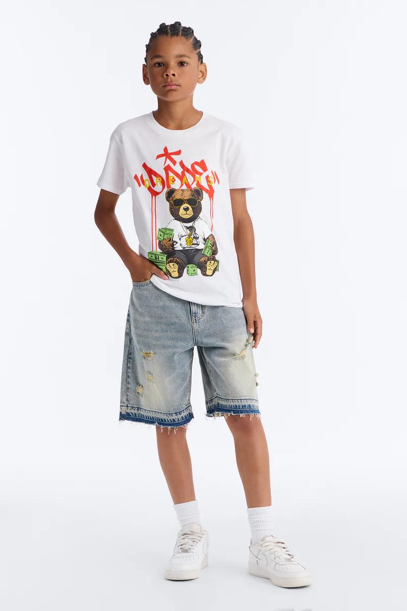 Niño con camiseta blanca de oso de peluche, shorts vaqueros desgastados y zapatillas. Moda juvenil.